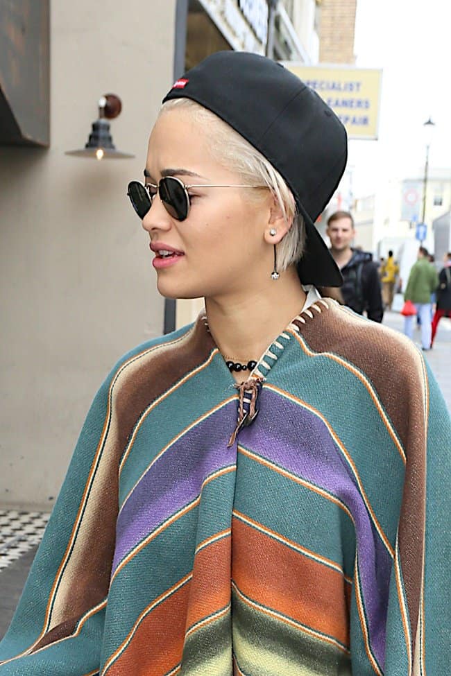 Rita Ora in a striking and bold striped poncho and a cap worn backwards